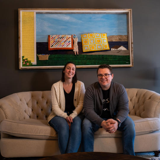 Owners Jonathan and Liz sit in front a large piece of their art