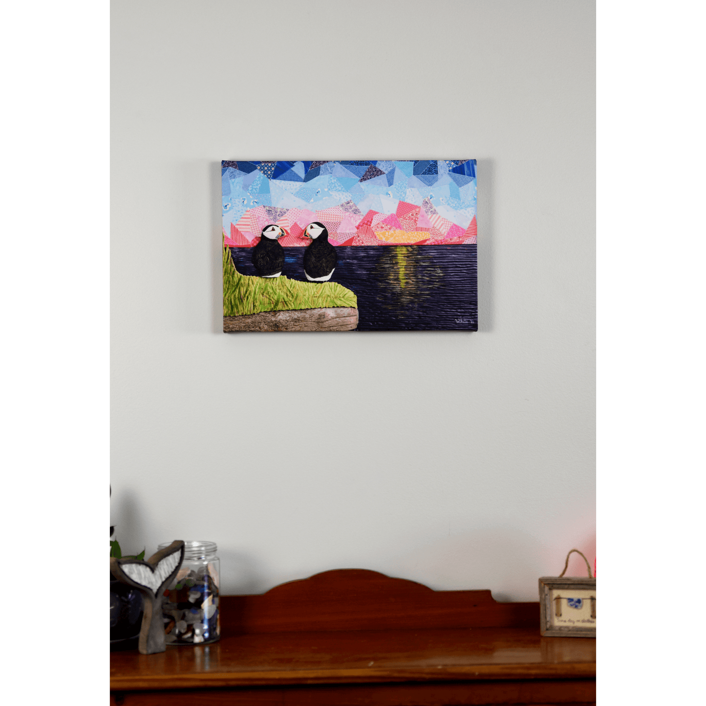 "The Perfect View" reproduction canvas showcases two puffins perched on a coastal rock, gazing lovingly at each other while enjoying a sunset over the ocean.