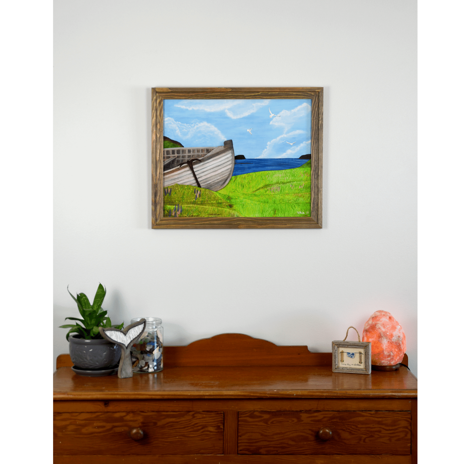 "New Beginnings" is a print featuring a wooden fishing boat that sits on a green Newfoundland shore with the ocean and seagulls in the background.