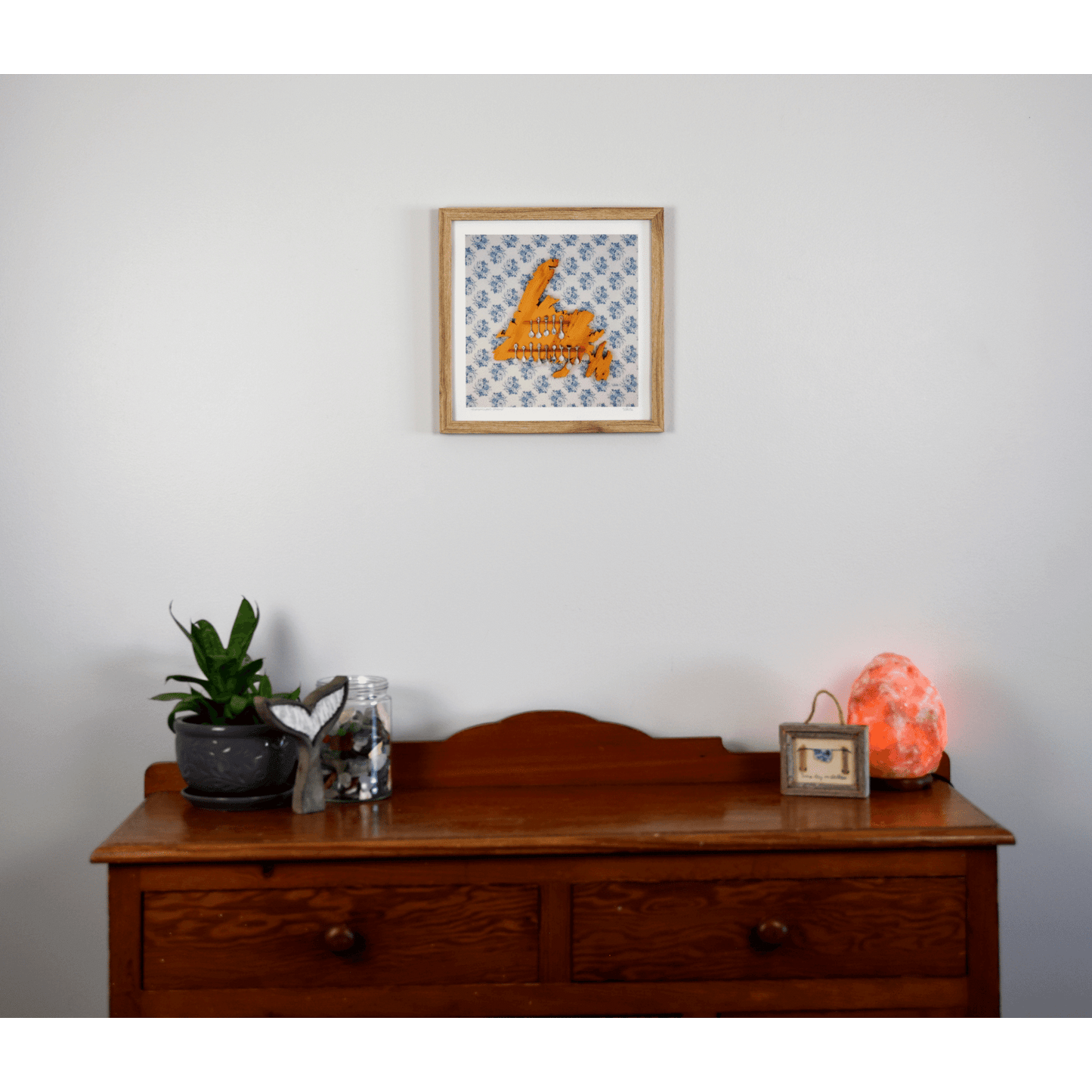 "Newfoundland Spoons" reproduction print showcases a wooden Newfoundland island spoon holder hanging on a flowery wallpapered wall.