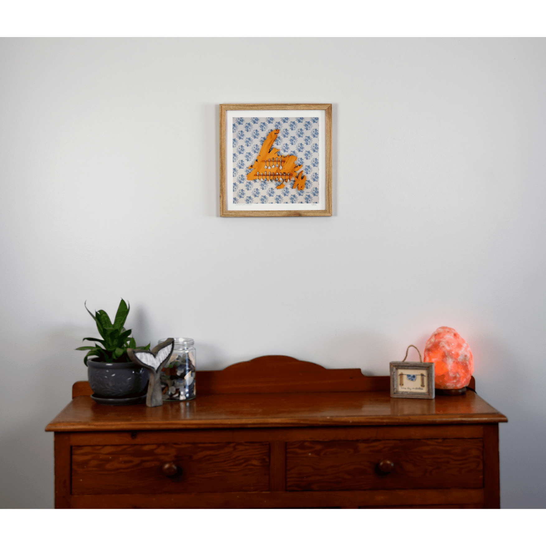 "Newfoundland Spoons" reproduction print showcases a wooden Newfoundland island spoon holder hanging on a flowery wallpapered wall.