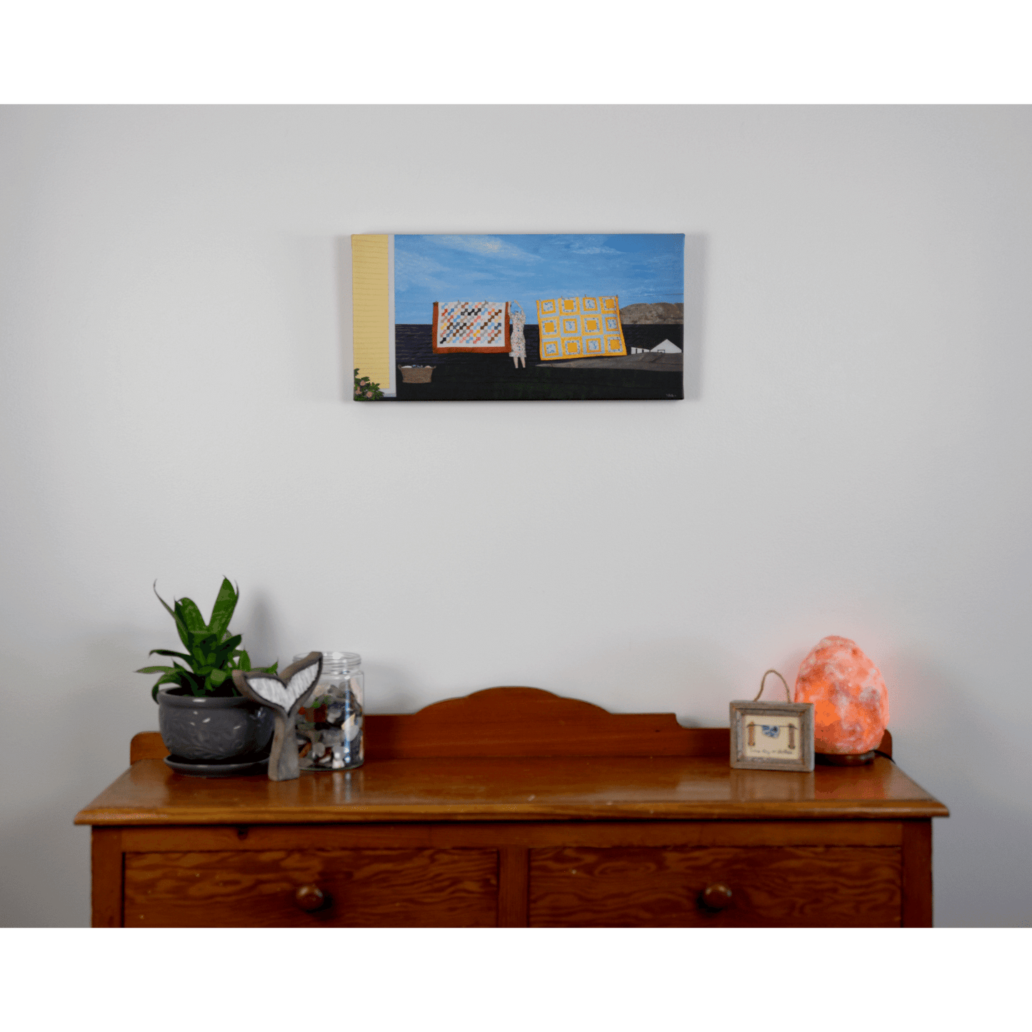 "Quilts" canvas print features a woman in a yellow dress hanging quilts with the ocean and Twillingate coast in the background.