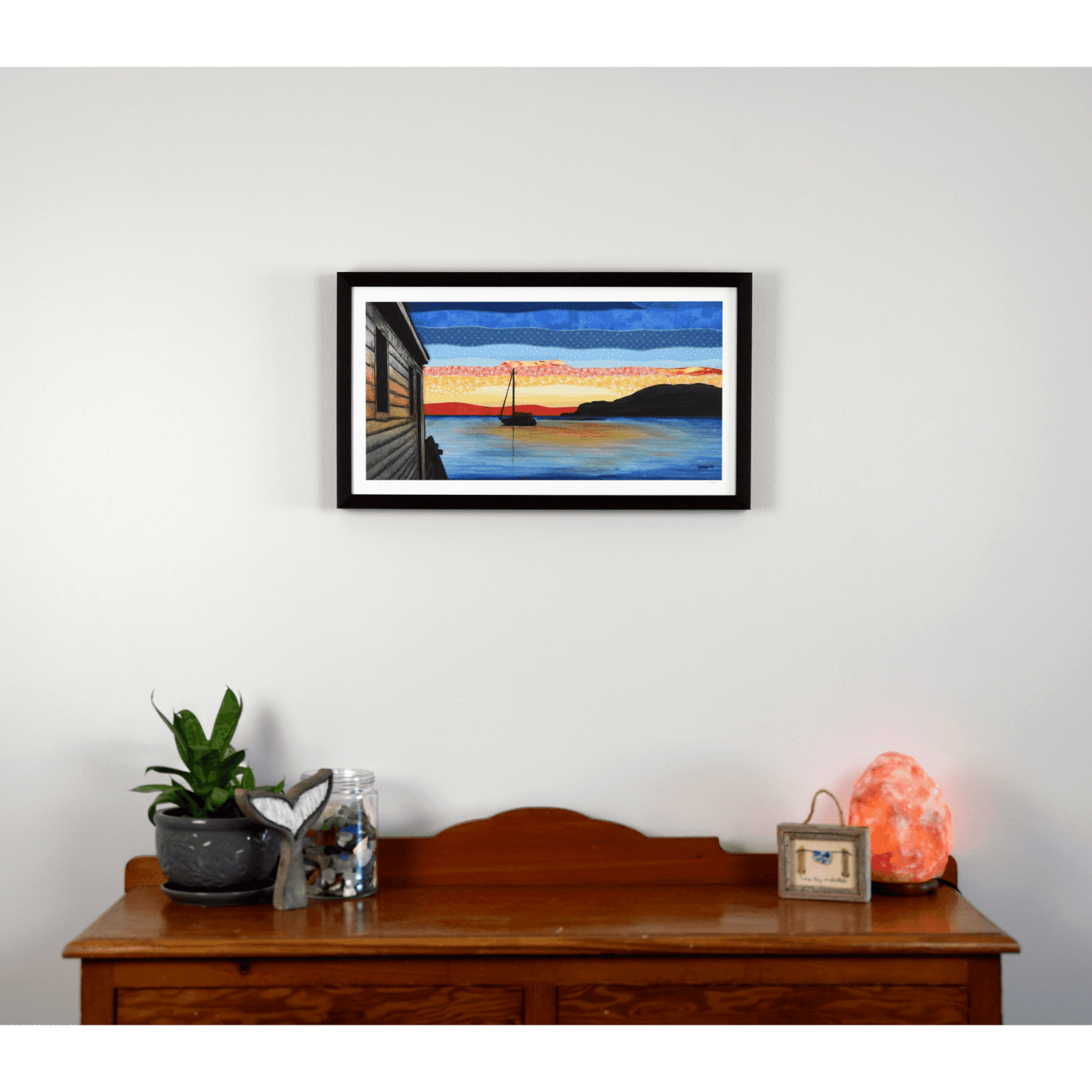 "Silhouettes" is a reproduction print that depicts a sailboat at sunset in Back Harbour, Twillingate. The red and orange hues are reflected in the calm ocean.