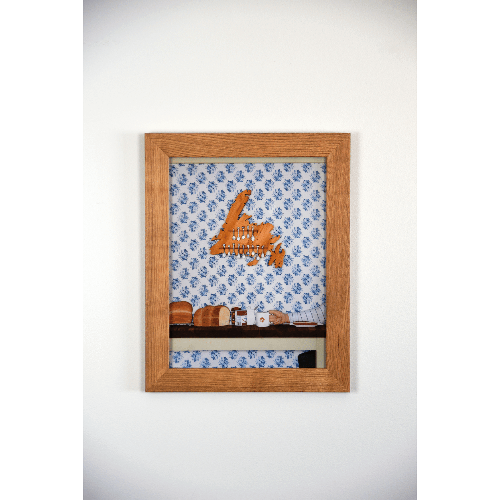 "Stealing the Healtap" print captures the warmth of a cozy family meal at Nan's, with bread, a mug, and a wooden spoon holder shaped like Newfoundland.