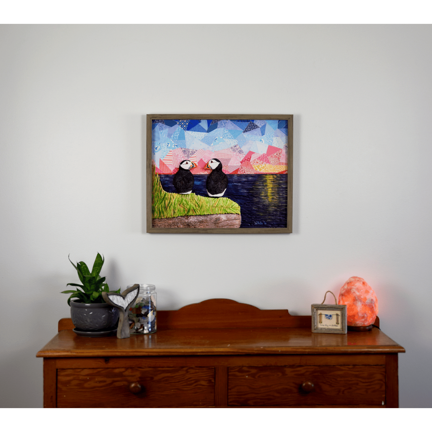 "The Perfect View" reproduction print showcases two puffins perched on a coastal rock, gazing lovingly at each other while enjoying a sunset over the ocean.