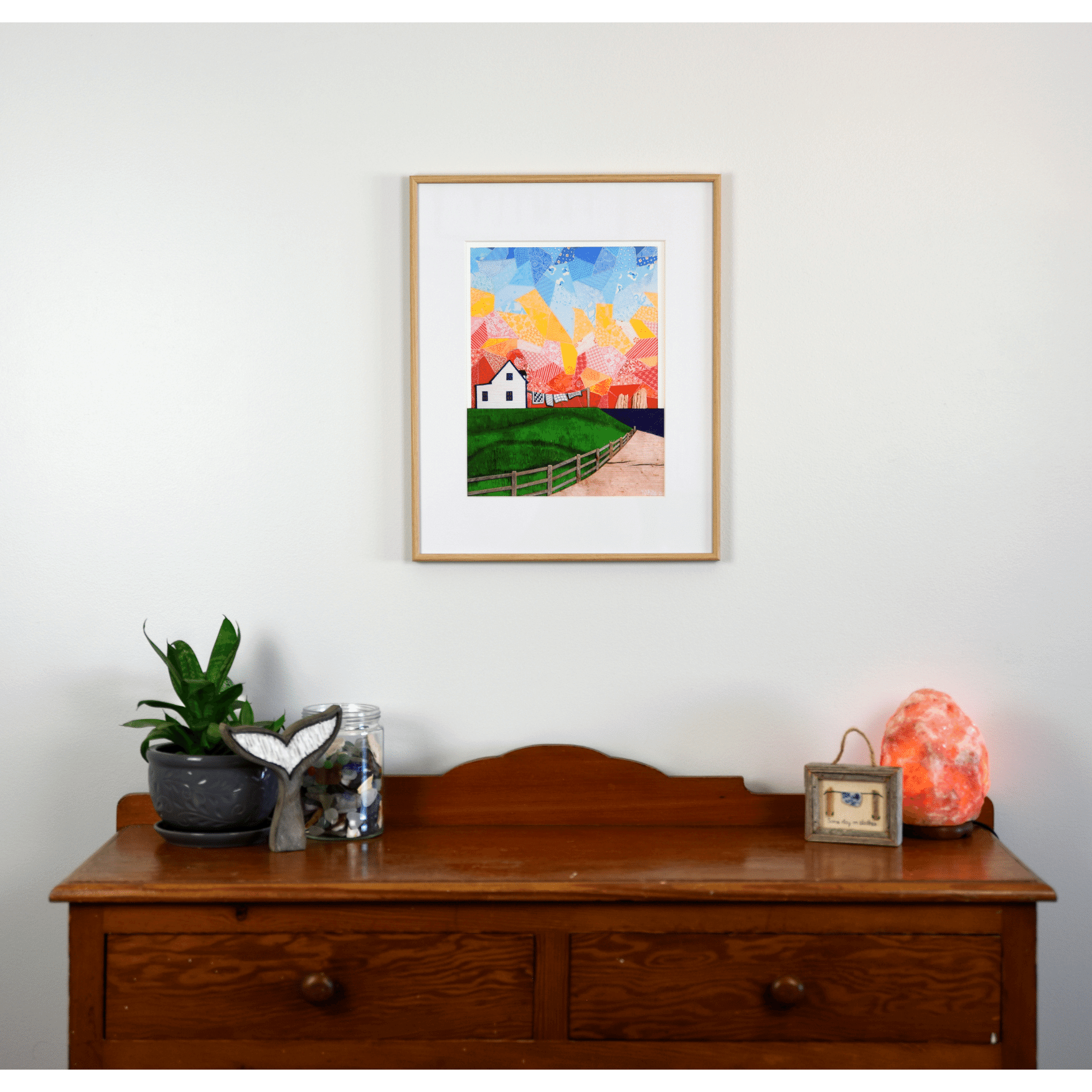 "Twillingate Sunrise" is a serene reproduction print showcasing a house against a patchwork pink and orange sky, with a green lawn and ocean in the foreground.