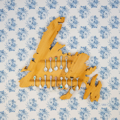 "Newfoundland Spoons" reproduction print showcases a wooden Newfoundland island spoon holder hanging on a flowery wallpapered wall.