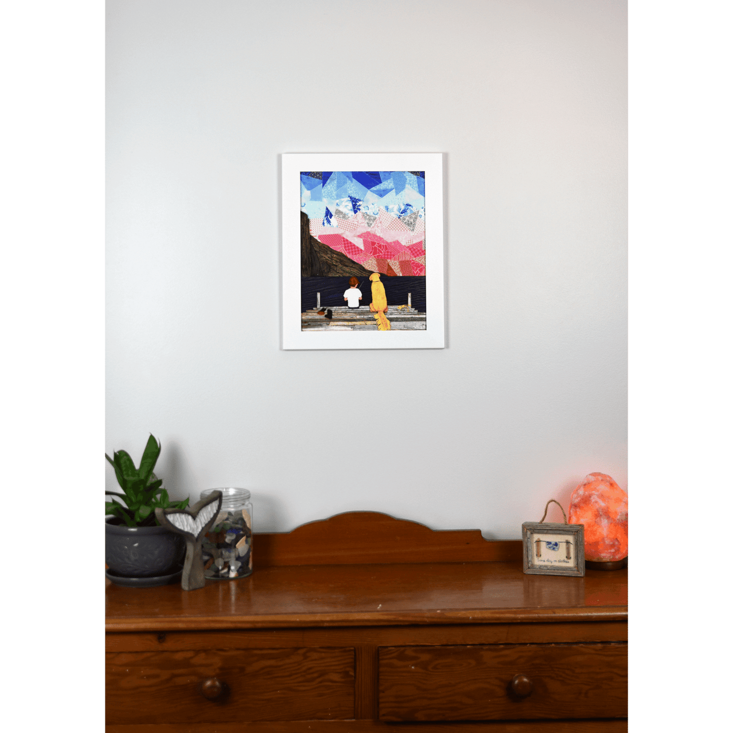 "A Boy and his Dog" print showcases a serene image of a boy sitting on a pier with his loyal yellow Labrador beside him, set against an ocean and sky backdrop.