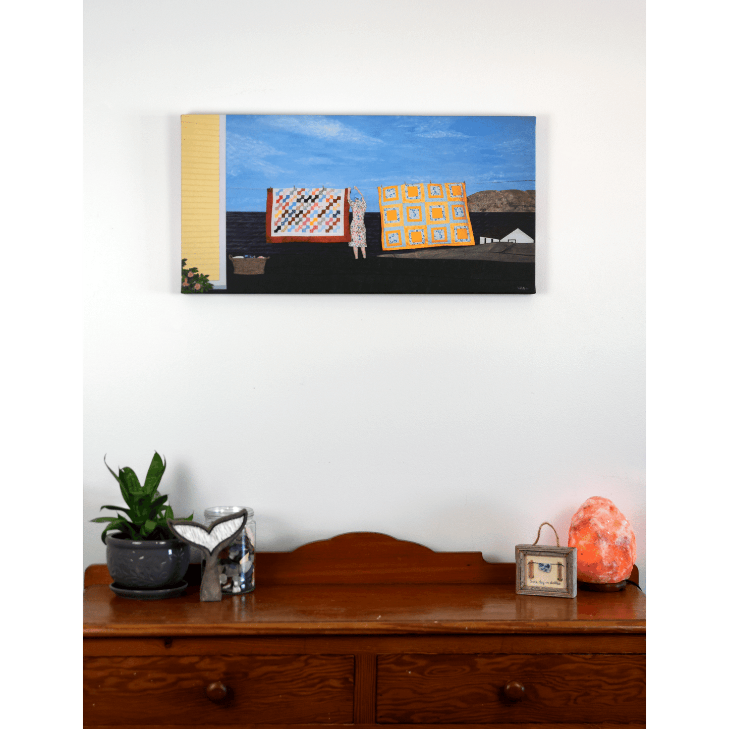 "Quilts" canvas print features a woman in a yellow dress hanging quilts with the ocean and Twillingate coast in the background.
