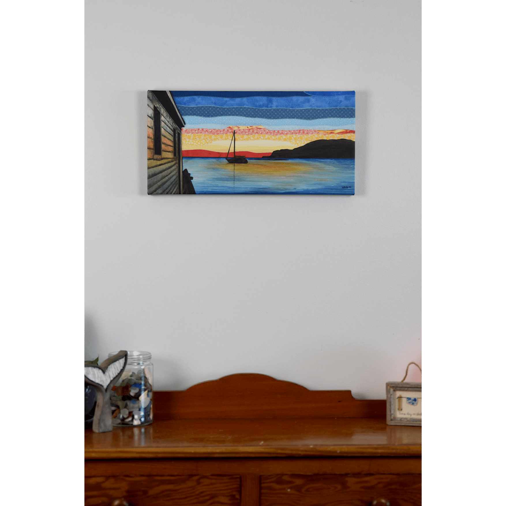 "Silhouettes" is a reproduction canvas that depicts a sailboat at sunset in Back Harbour, Twillingate. The red and orange hues are reflected in the calm ocean.