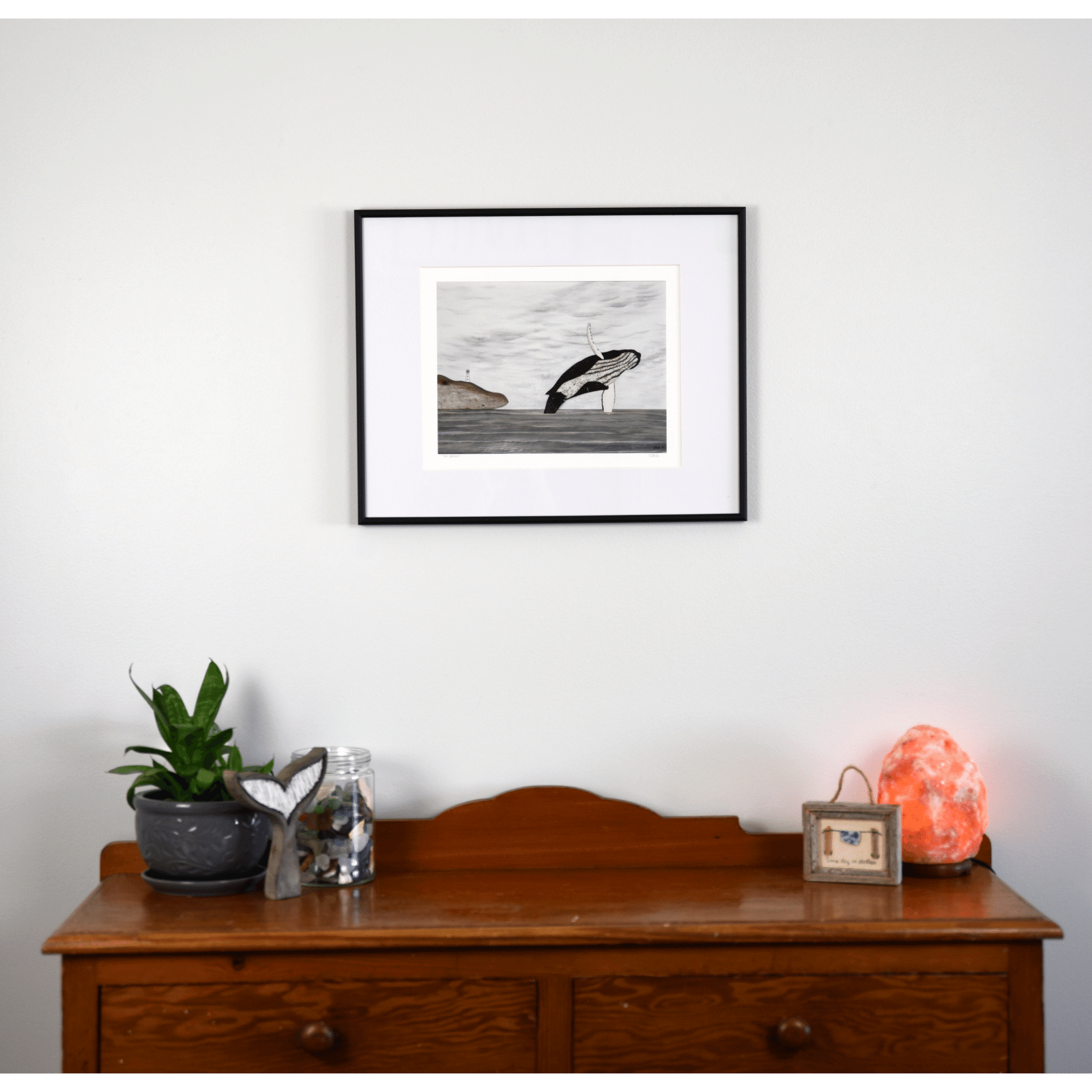  "The Breach" is a print capturing a humpback whale breaching out of the ocean near Newfoundland's shores with a hill and a lighthouse in the background.