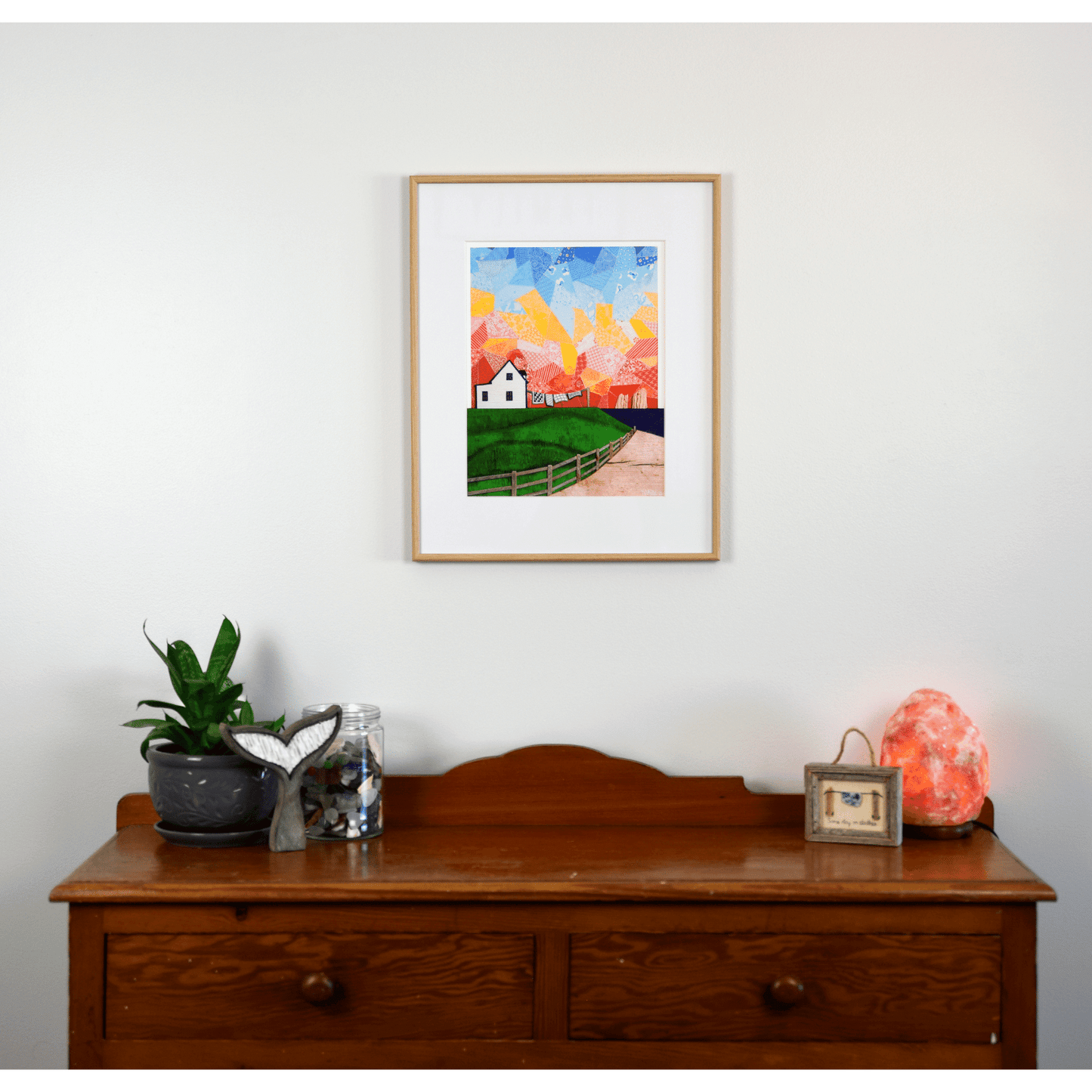  "Twillingate Sunrise" is a serene reproduction print showcasing a house against a patchwork pink and orange sky, with a green lawn and ocean in the foreground.  