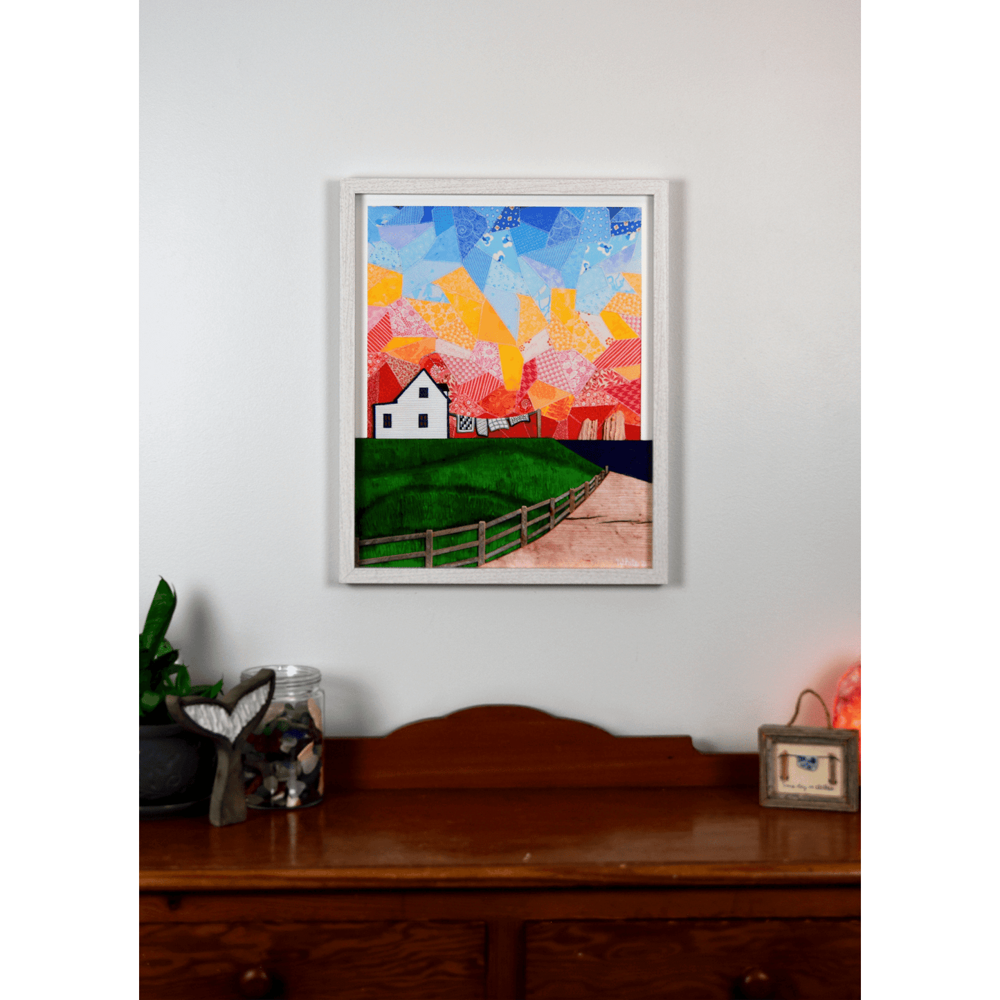  "Twillingate Sunrise" is a serene reproduction print showcasing a house against a patchwork pink and orange sky, with a green lawn and ocean in the foreground.  